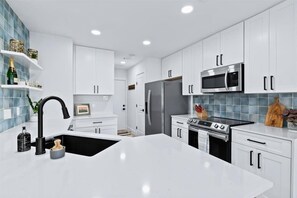 A modern kitchen with white cabinetry, a central island, a stainless steel refrigerator, and a microwave. - Charming Urban Home with pet friendly backyard (Austin)