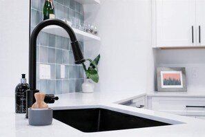 A modern kitchen with a black faucet, a marble bottle, a small plant, and a framed picture on the wall. - Charming Urban Home with pet friendly backyard (Austin)