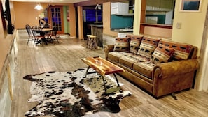 Una sala de estar con un sofá, una mesa de centro de madera, un tapete de cuero de vaca y un comedor con sillas y una mesa.