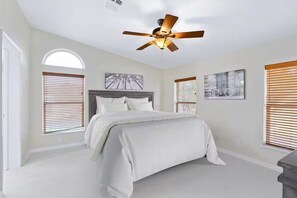 Une chambre à coucher avec un lit, un ventilateur de plafond et deux fenêtres équipées de stores.