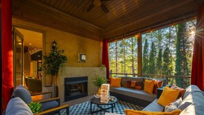 A cozy room with a fireplace, a sofa with cushions, a coffee table, and a view of trees through large windows. - Sleeps 20 • 15 Mins to DT AVL • Sauna • Hot Tub! (Fletcher)