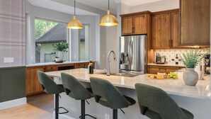 A modern kitchen with a central island, bar stools, wooden cabinets, stainless steel appliances, pendant lighting, and a view of the outdoors. - Sleeps 20 • 15 Mins to DT AVL • Sauna • Hot Tub! (Fletcher)