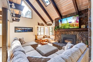 A cozy living room with a stone fireplace, a large flat-screen TV, and a comfortable seating area. - The Village Nook at Backwoods, Short Walk to the Village, AC, SHARC, Grill, Pets (Sunriver)