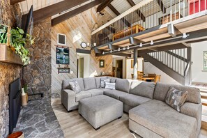 Un vaste espace de vie agrémenté d’une cheminée en pierre, d’un grand canapé d’angle et d’un plafond en bois.