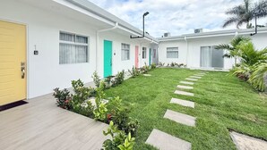 Un bâtiment moderne avec une porte jaune, une porte verte et une porte rose. Une pelouse bien entretenue s’étend devant le bâtiment, et des pierres plates permettent d’accéder à l’entrée.