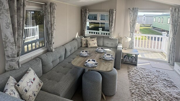 A cozy living area with a sofa, a dining table set with plates, and a view of a balcony. - Golden Palm Resort - Palm Skye PG155 (Chapel Saint Leonards)