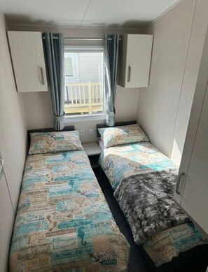 Une petite cabine avec deux lits, une fenĂȘtre avec des rideaux et une vue sur la terrasse extĂ©rieure.