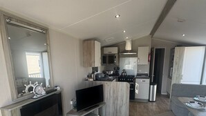 A modern kitchen with a flat-screen TV, wooden cabinets, and a stainless steel refrigerator. - Golden Palm Resort - Palm Skye PG155 (Chapel Saint Leonards)