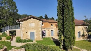 Un bâtiment en pierre doté d’un balcon, d’un chemin et d’un grand arbre.