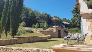 Un bâtiment en pierre doté d’une terrasse, d’un mur en pierre et d’un espace verdoyant avec des arbres.