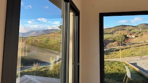 Una habitación con un ventanal que ofrece vistas a un paisaje rural con colinas y una casa.