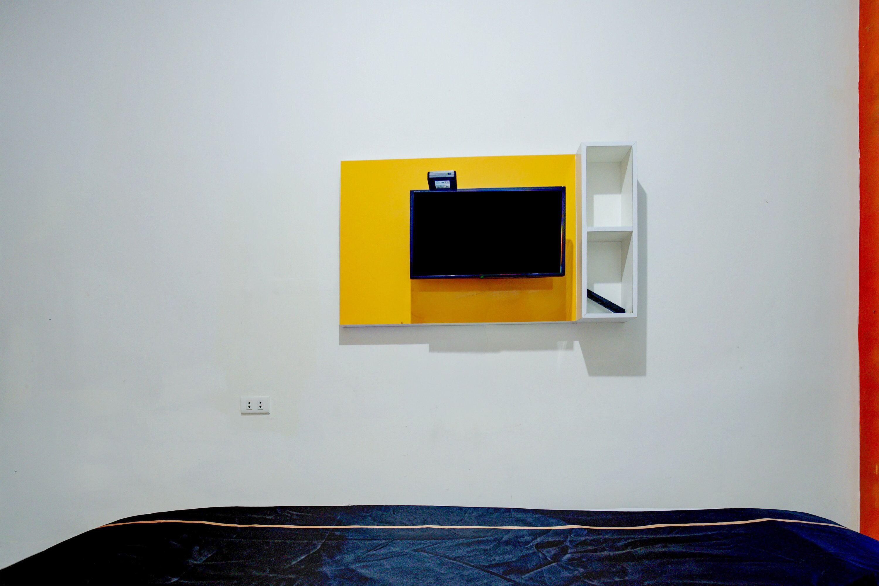 A room with a bed, a wall-mounted TV, and a white shelf unit.