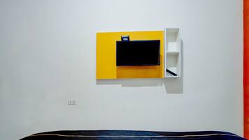 A room with a bed, a wall-mounted TV, and a white shelf unit.