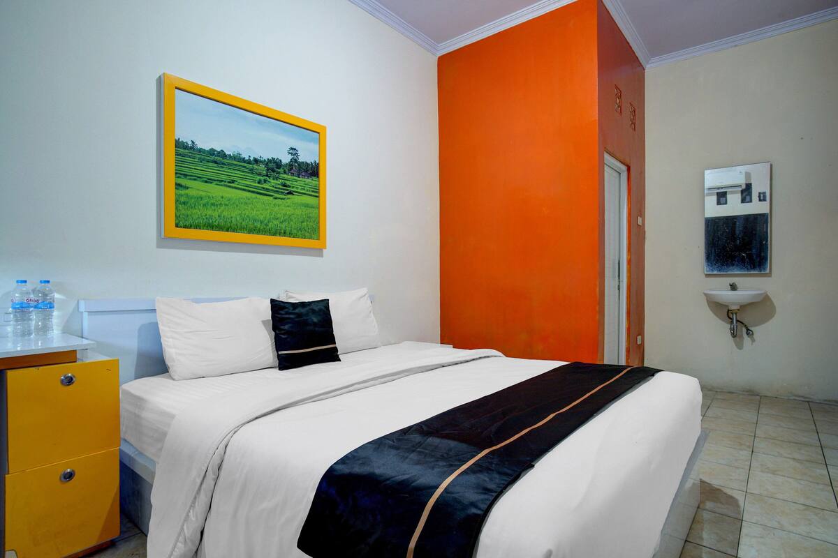 Una habitación de hotel con una cama, una mesita de noche, un cuadro enmarcado, un lavabo y una puerta.