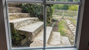 A window with a view of stone steps leading to a white picket fence.