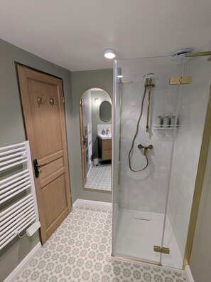 A bathroom with a glass shower enclosure, a wooden door, and a patterned floor. - Romantic hideaway in Jumilhac: The Nest, a riverside gem near the château (Jumilhac-le-Grand)