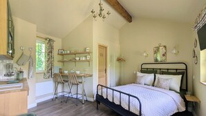 A bedroom with a bed, a desk with chairs, and a kitchenette.