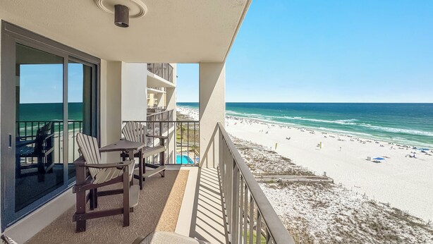 Un balcone con vista sulla spiaggia, una piscina e un'area pranzo con sedie e tavolo.