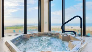 Una vasca idromassaggio con decorazioni in marmo, un rubinetto nero e vista sulla spiaggia attraverso ampie finestre.