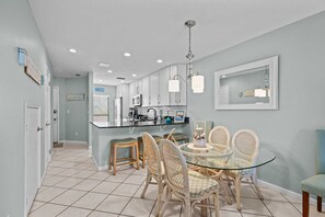 Una cocina moderna con una isla central, taburetes de bar y una mesa de comedor con sillas de mimbre.