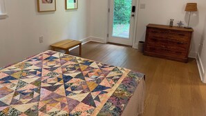 Ein Schlafzimmer mit einem Bett, einem Schminktisch, einer zur Außenseite führenden Tür und zwei gerahmten Bildern an der Wand.