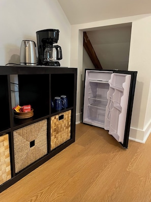 Un espace cuisine compact comprenant une machine à café, une bouilloire et des paniers de rangement.