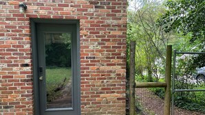 Ein Backsteinhaus mit einer dunklen Tür, einer kleinen Veranda und einem Holzzaun.