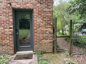 A brick building with a dark door, a small porch, and a wooden fence.