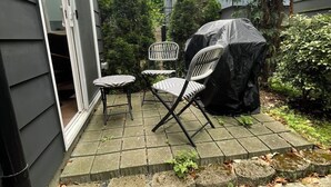 Een terras met buitenmeubilair, een barbecue en een klein waterpartij.
