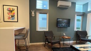 Een moderne woonkamer met een televisie, twee fauteuils, een rode bank, een klein tafeltje en een barretje.