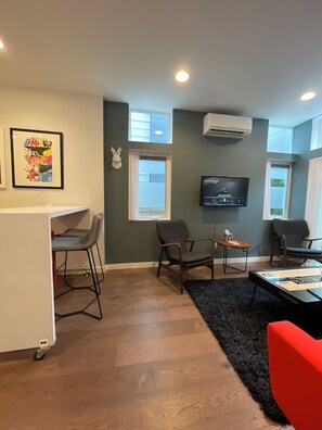 Ein modernes Wohnzimmer mit Fernseher, zwei Sesseln, einem roten Sofa, einem kleinen Tisch und einer Bar.