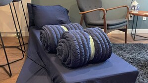 Een moderne kamer met een eenpersoonsbed, een grijze fauteuil, een houten nachtkastje en een televisie.