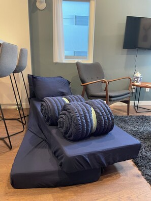 Ein modernes Zimmer mit einem Einzelbett, einem grauen Sessel, einem Holztischchen und einem Fernseher.