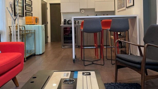 Een ruimtelijk ingerichte leefruimte met kitchenette, een rode bank, een blauw vloerkleed en een barstoelgedeelte.