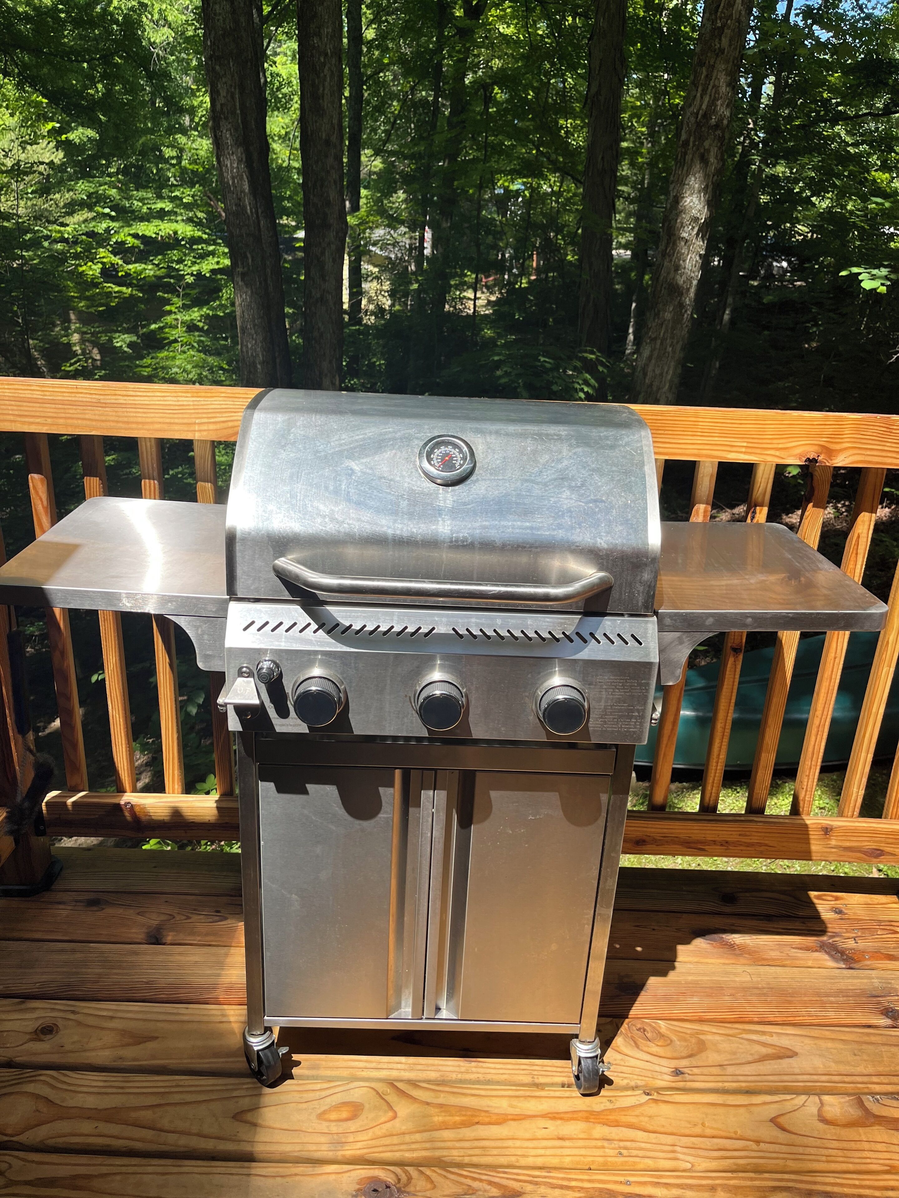 A stainless steel barbecue grill with a digital thermometer, adjustable knobs, and a side burner, set on a wooden deck with a railing.