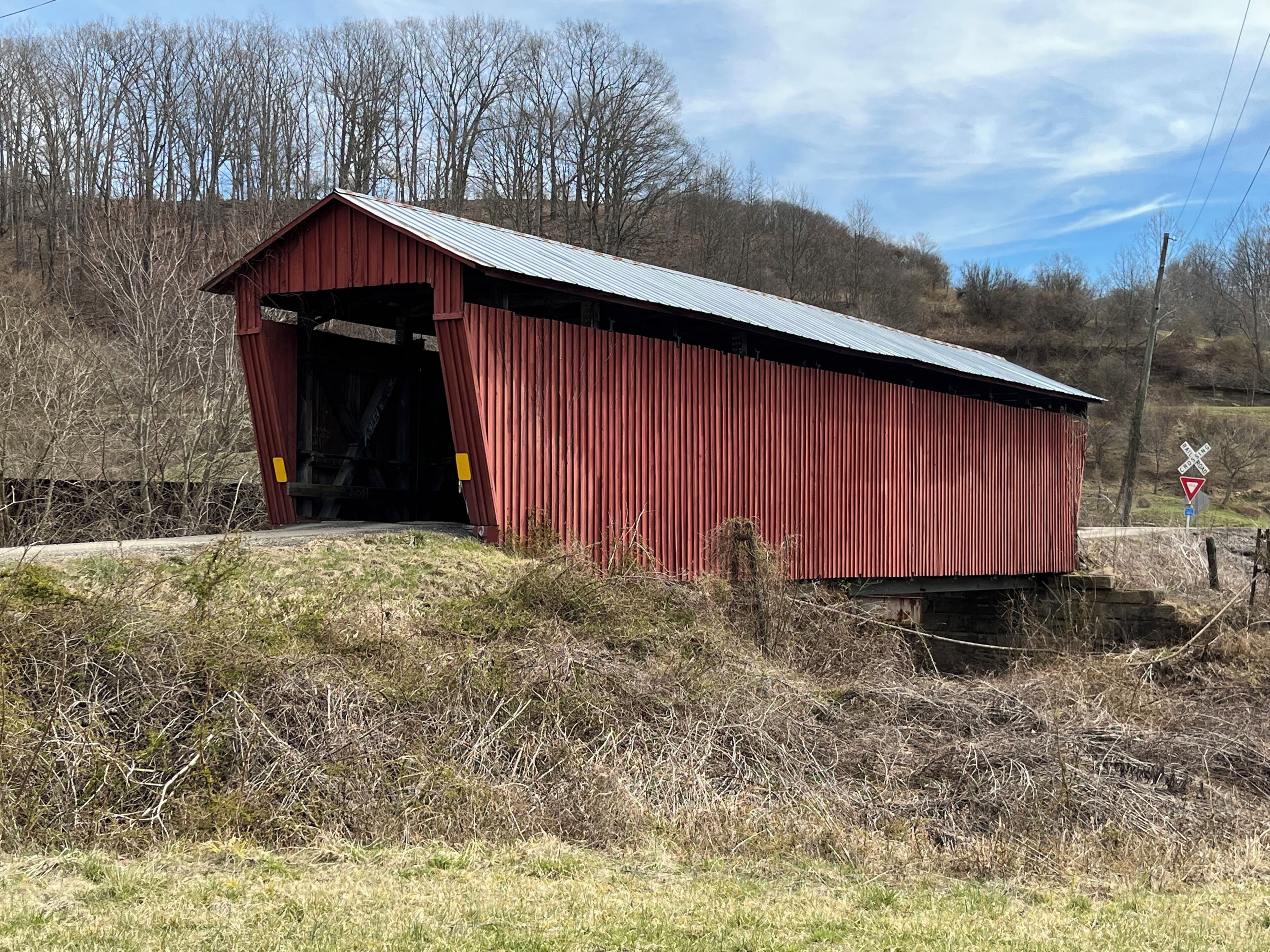 Eine rote gedeckte Brücke mit einem Metalldach, umgeben von trockenem Gras und Bäumen.