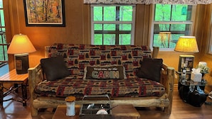 Een knus kamer in blokhutstijl met een gestreept sofa, een houten bijzettafeltje en een raam met uitzicht op groen.