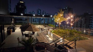 An outdoor terrace with tables and chairs, a staircase, and a city skyline in the background. - Flat Sol & Praia Move Tambaú (João Pessoa)