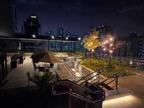 An outdoor terrace with tables and chairs, a staircase, and a city skyline in the background. - Flat Sol & Praia Move Tambaú (João Pessoa)