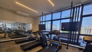 A gym with treadmills, exercise equipment, and large windows with a city view. - Flat Sol & Praia Move Tambaú (João Pessoa)