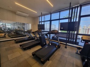 A gym with treadmills, exercise equipment, and large windows with a city view. - Flat Sol & Praia Move Tambaú (João Pessoa)