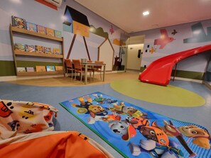 Un espace de jeux pour enfants avec un toboggan, des tapis de jeu colorés et une bibliothèque remplie de livres pour enfants.