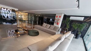 A modern living room with a large sofa, a round coffee table, and a green ottoman. There is a glass wall with a sign that reads 'MOVE'. - Flat Sol & Praia Move Tambaú (João Pessoa)