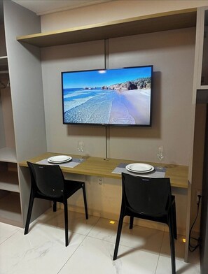 Comedor con televisión instalada en la pared mostrando una escena de playa, dos sillas y una mesa preparada para dos personas.