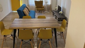 Ein Essbereich mit einem Holztisch, gelben Stühlen, einem blauen Sofa und einer gelben Tür.