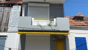 Ein zweigeschossiges Gebäude mit gelber Tür, geschlossenem Rollladen und einem Balkon.