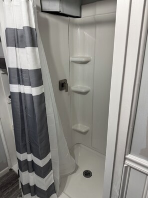 A shower with a white tiled wall, a drain, and a door with a silver handle.
