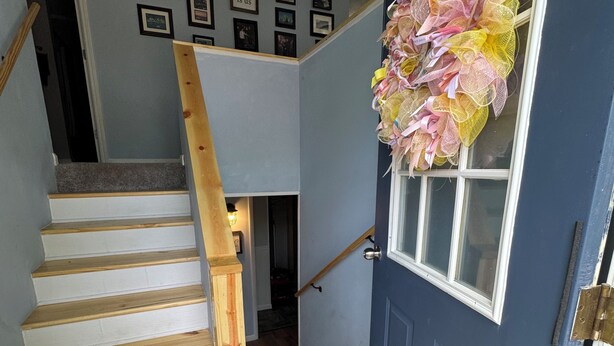 Una escalera que lleva a una habitación con una puerta azul, una pared con cuadros enmarcados y una ventana con un adorno decorativo.