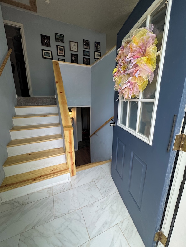 A staircase leading to a room with a blue door, a wall with framed pictures, and a window with a decorative wreath.