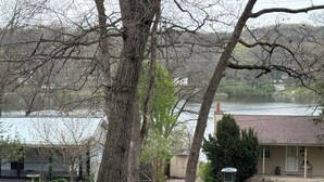 Zona residencial con un árbol grande, una casa con porche y una masa de agua al fondo.